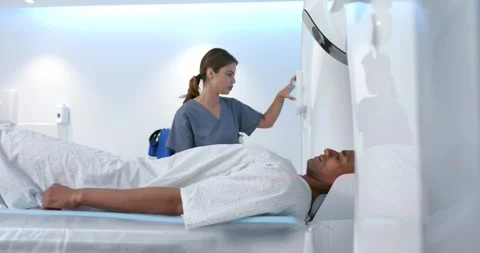 African American man lying in scanner after alignment, tech in scrubs operating Stock Footage 334841966