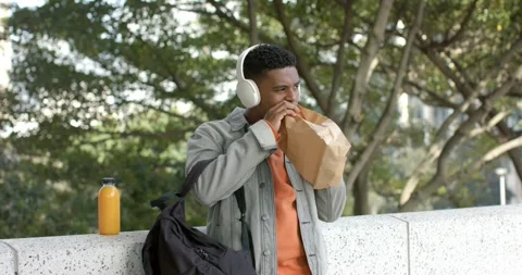 African American man placing backpack, juice on ledge opening bag eating Stock Footage 337704895