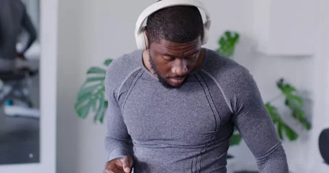 African American man placing headset at gym adjusting grabbing phone tapping app Stock Footage 340654655