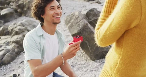 African american man proposing his girlfriend with a ring on the rocks near the Stock Footage 340971418