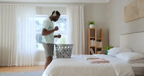 African American man pulling clothes from gray laundry basket folding on bed Stock Footage 343889015