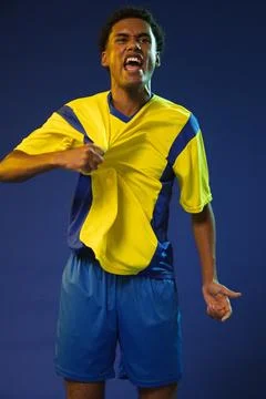 African American man pulling yellow blue soccer kit, shouting in studio lighting Stock Photos