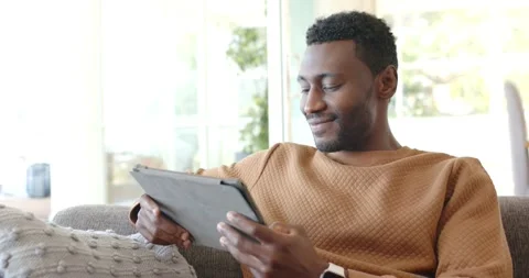 African American man scrolling tablet after notification popping up on living Stock Footage 341932058