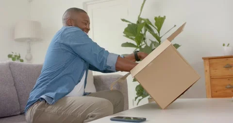 African American man seeing package at home lifting opening inspecting inner box Stock Footage 340881914