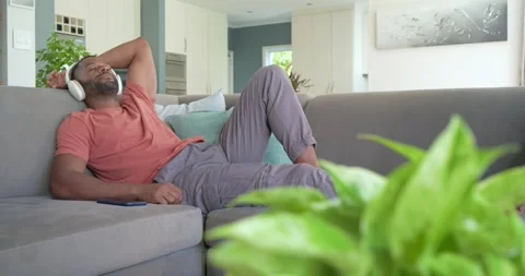 African American man settling back and resting on sofa in living room with Stock Footage 337624975