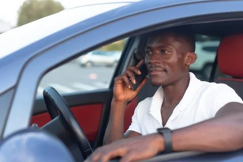 An African-American man sitting behind the wheel of a car with a phone in his Stock Photos