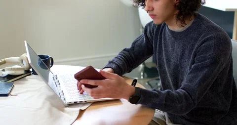 African American man sitting at round table, checking phone, typing on laptop Stock Footage 341027872