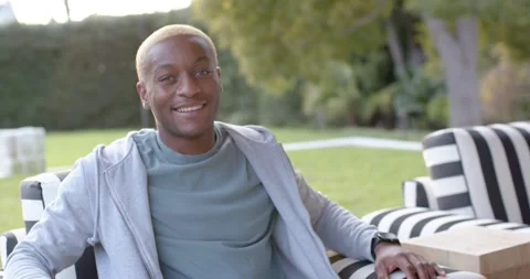 African American man smiling, making eye contact, reclining on striped chair as Stock Footage 345589602