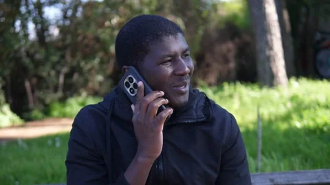 African American man smiling while talking on smartphone in park Stock Footage 332420603