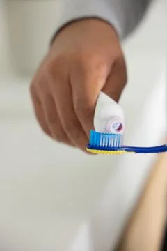 African American man squeezing paste from white tube onto blue toothbrush at Stock Photos