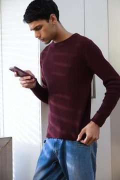 African American man standing using smartphone by white wardrobe, maroon sweater Stock Photos