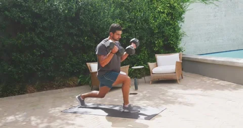 African American man starting with hex dumbbells doing lunges on poolside mat in Stock Footage 342113048