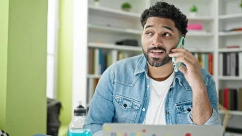 African american man student using laptop talking on smartphone at library .. Video stock 242899724