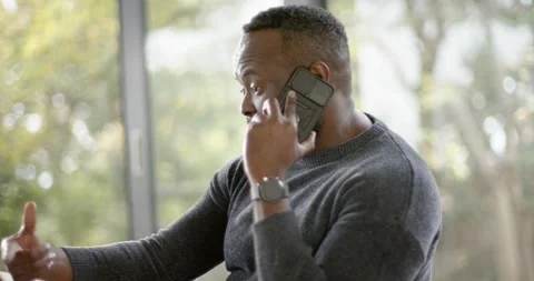 African American man at table answering work call on phone, reaching for tablet, Stock Footage 342363084