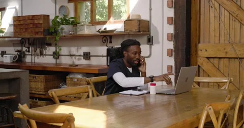 African American man taking call, typing laptop checking notes for work at Stock Footage 337400725