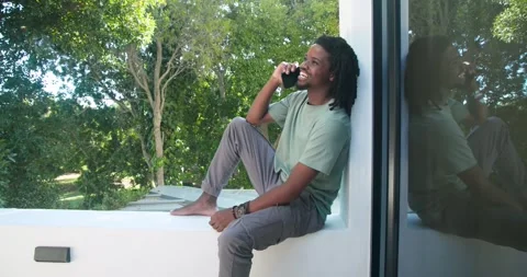 African American man taking ringing call on home ledge, chatting with friend on Stock Footage 342023508