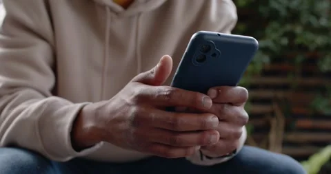 African American man tapping and scrolling blue phone with wristwatch on bench, Stock-Footage 345618341