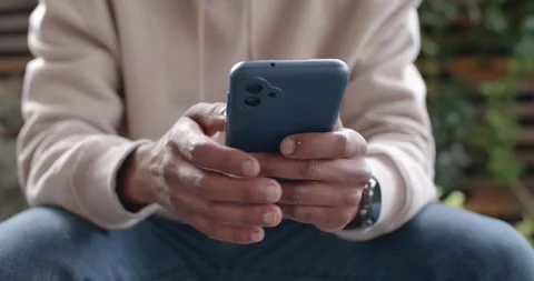 African American man tapping blue phone reading message and laughing on wooden Stock-Footage 345618333