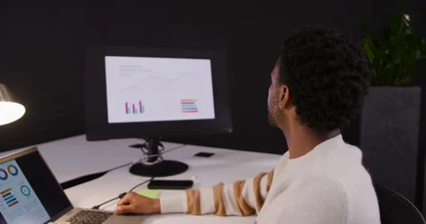 African American man turning to external monitor with charts, checking, updating Stock Footage 345607305