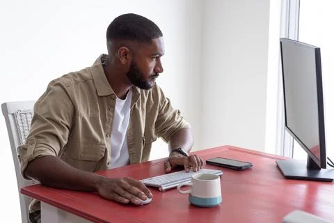 African american man using computer with wireless keyboard and mouse at desk at Stock Photos