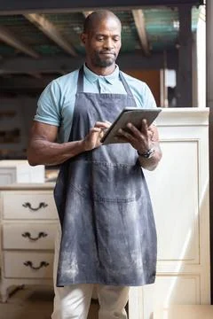African American man using digital tablet and inspecting wooden cabinets in Stock Photos