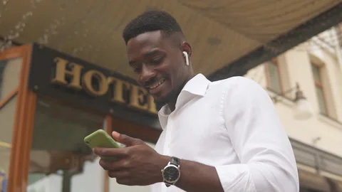 African american man using his smartphone standing outside hotel Stock Footage