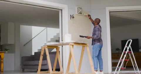 African American man using paintbrush from sawhorse tray, painting porch wall Stock Footage 336059646