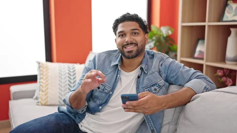 African american man using smartphone doing ok gesture at home Video stock 242900105