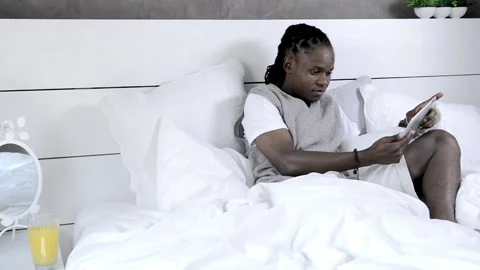 African american man using tablet computer in luxury bedroom Stockbeeldmateriaal 199629434