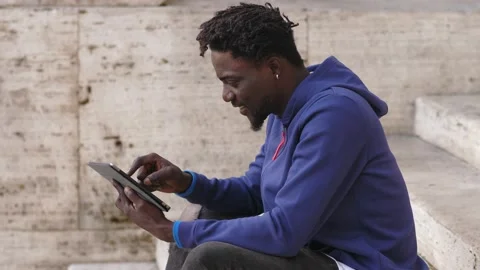 African american man using tablet while relaxing on a cafe on the stairs Stock Footage 218602698