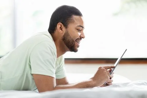 African american man using tablet in bed, using mobile app Foto stock