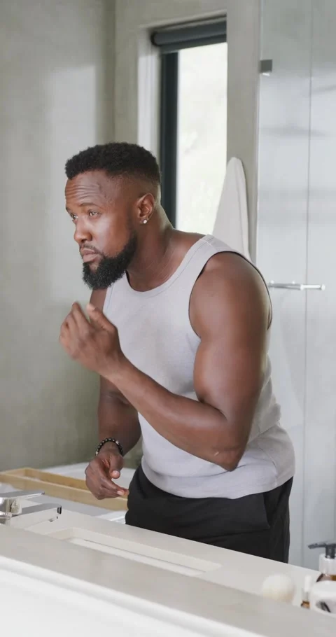 African American man at vanity looking at mirror rubbing face stroking beard Stock Footage 346719011