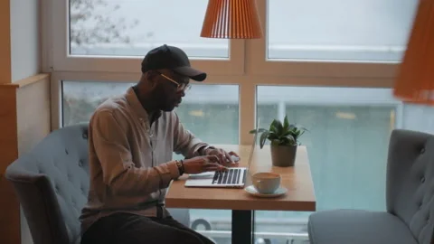 An African-American man works at a computer while sitting at a table in a cafe. Stock Footage 263057032
