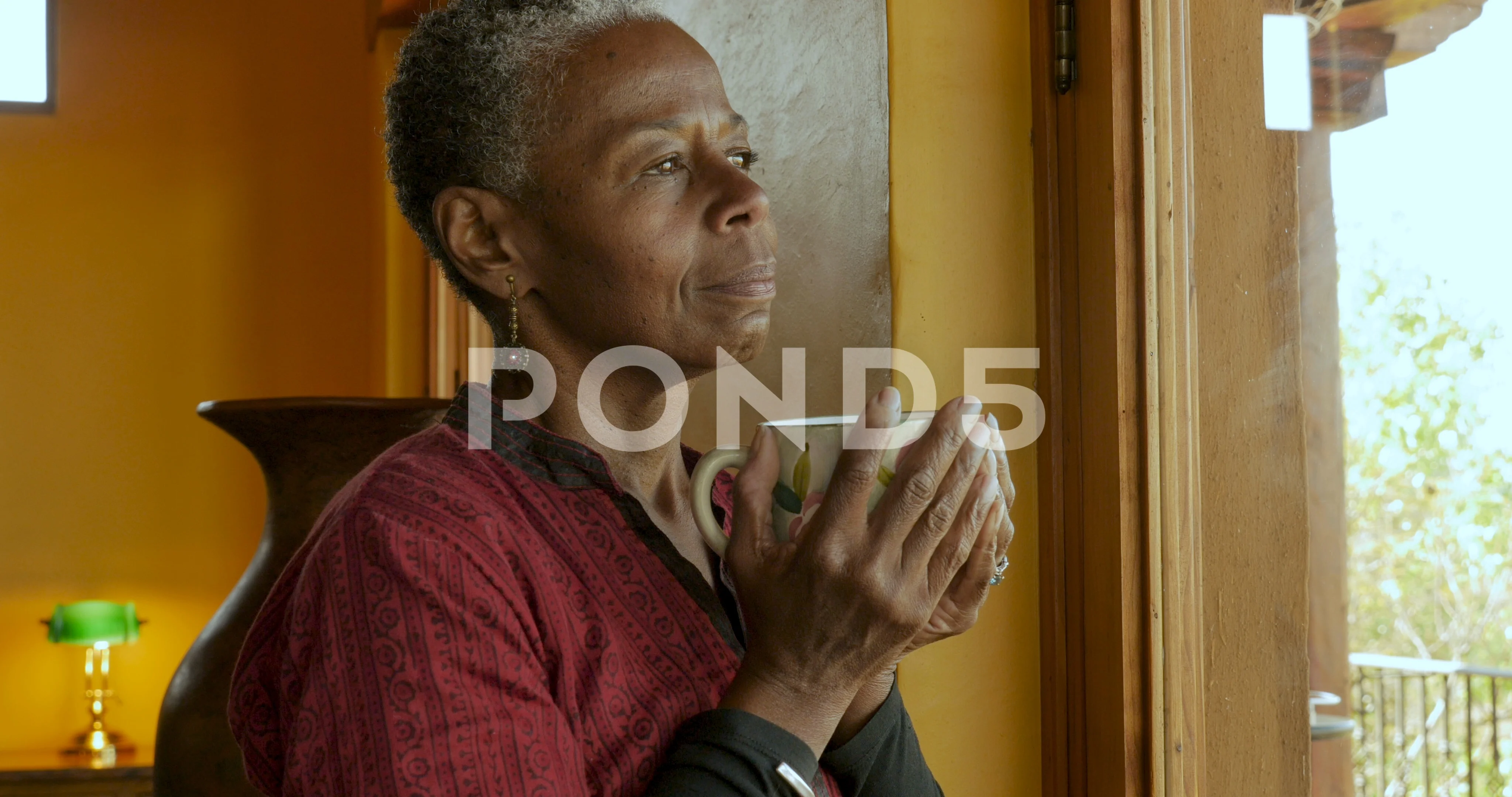 African American mature woman drinking coffee while looking out a window