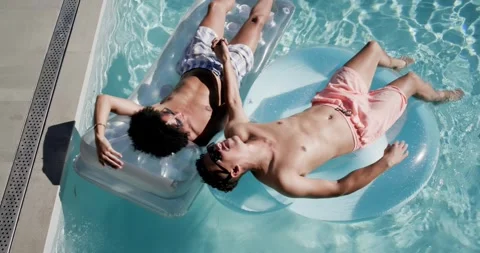 African American men floating on pool floats holding hands, showing love while Stock Footage 339272530