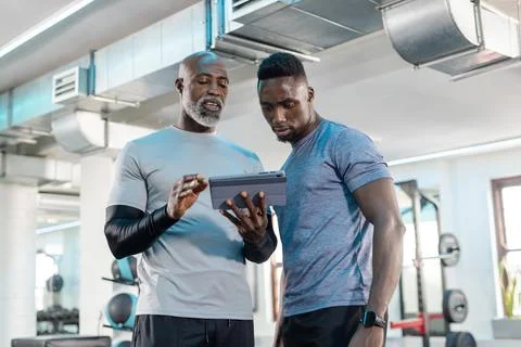 African American men studying workout data on tablet at fitness center with 스톡 사진