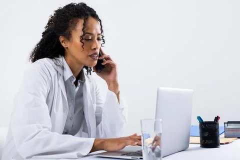 African american mid adult woman talking over smart phone and using laptop on Stock Photos