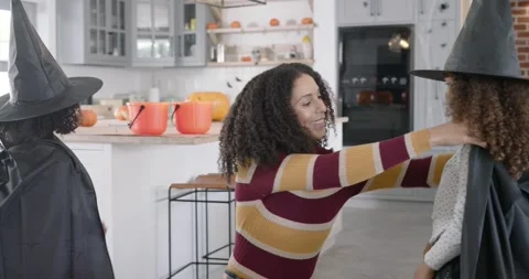 African American mom adjusting two girls' witch capes passing pumpkin buckets in Stock Footage 345088117