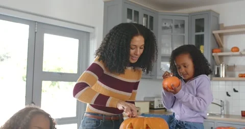 African American mom scooping pulp while girls decorating pumpkins at kitchen Stock Footage 345086879