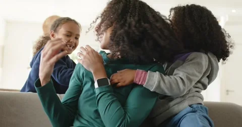 African American mom with two daughters climbing onto couch and tickling Stock Footage 345087941