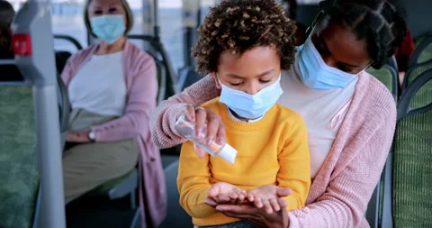 African-american mother with covid mask disinfecting boy hands inside bus Stock Footage