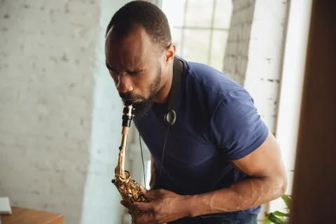 African-american musician playing saxophone during online concert at home Stock Photos