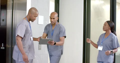 African American nurses exiting elevator as colleague hurrying with tablet, Stock Footage 334999897