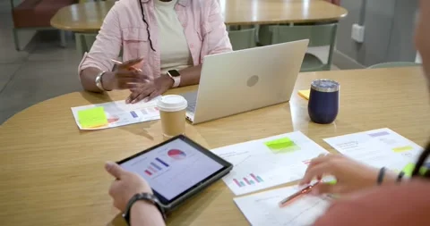 African American pair annotating charts at table, man shifting tablet toward 库存影片 334999913