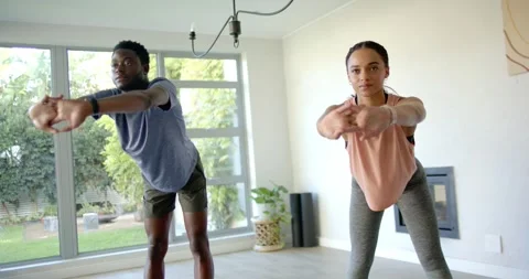 African American pair holding synchronized squat at home near window, following Stock Footage 339560043