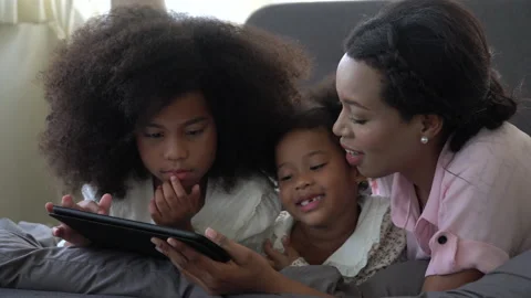 African american single mom with two daughter lying down on bed looking table Stock Footage 136740421