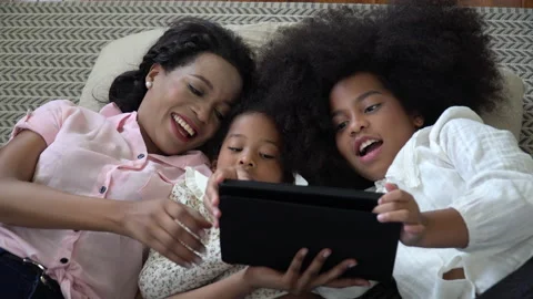 African american single mom with two daughter lying down on bed looking table Stock Footage 136740799