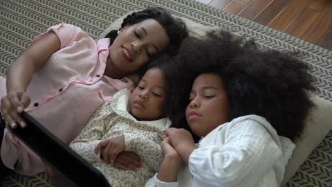 African american single mom with two daughter lying down on bed looking table Stock Footage 136740929