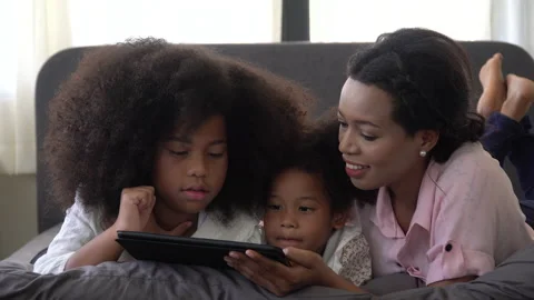 African american single mom with two daughter lying down on bed looking table Stock Footage 136740991