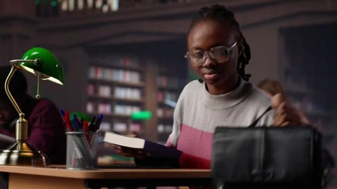African american student comparing class notes with data from the library Stock Footage 308713477
